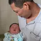 Tran Van Quan menggendong bayi laki-lakinya, Tran Tien Quoc di pusat kesehatan Vinh Tuong, provinsi Vinh Phuc, Vietnam, Minggu (15/10). Bayi laki-laki tersebut lahir melalui operasi Caesar pada 14 Oktober 2017 lalu. (LE PHUONG/AFP)