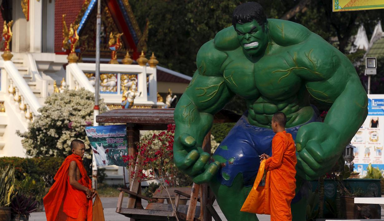 Dua orang biksu berpose di dekat patung "Hulk" di kuil Tamru di Samut Prakan, Thailand (3/3). Pihak Candi mengatakan telah menyiapkan patung-patung karakter komik Marvel untuk menarik pengunjung. (REUTERS/Chaiwat Subprasom)