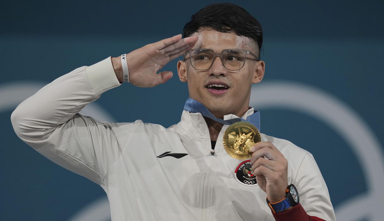 Atlet angkat besi Indonesia peraih medali emas kelas 73 kg putra cabor angkat besi Olimpiade Paris 2024, Rizki Juniansyah memberi hormat sambil menyanyikan lagu kebangsaan Indonesia Raya saat upacara penyerahan medali di Paris Expo Porte de Versailles, Paris, Kamis (8/8/2024). (AP Photo/Kin Cheung)