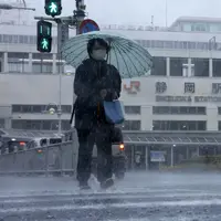 Seseorang berjalan di tengah hujan di depan sebuah stasiun di Shizuoka, sebelah barat Tokyo, Sabtu (13/8/2022). Badai Tropis Meari mengeluarkan hujan lebat di barat daya Jepang saat menuju ke utara menuju ibu kota Tokyo, menurut pejabat cuaca Jepang. (Kyodo News via AP)