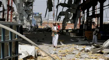 Seorang pria menggendong anaknya di sebuah bangunan pabrik pipa dan pompa air yang hancur akibat serangan udara Arab Saudi di Sanaa, Yaman, Kamis (15/9). Dalam serangan ini tidak ada korban jiwa. (REUTERS/Khaled Abdullah)