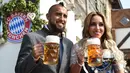 Gelandang Bayern Munchen, Arturo Vidal dan istrinya, Maria Teresa Matus memegang cangkir bir saat mereka berpose selama festival bir Oktoberfest 2017 di Munich, Jerman (23/9). (AFP Photo/Christof Stache)