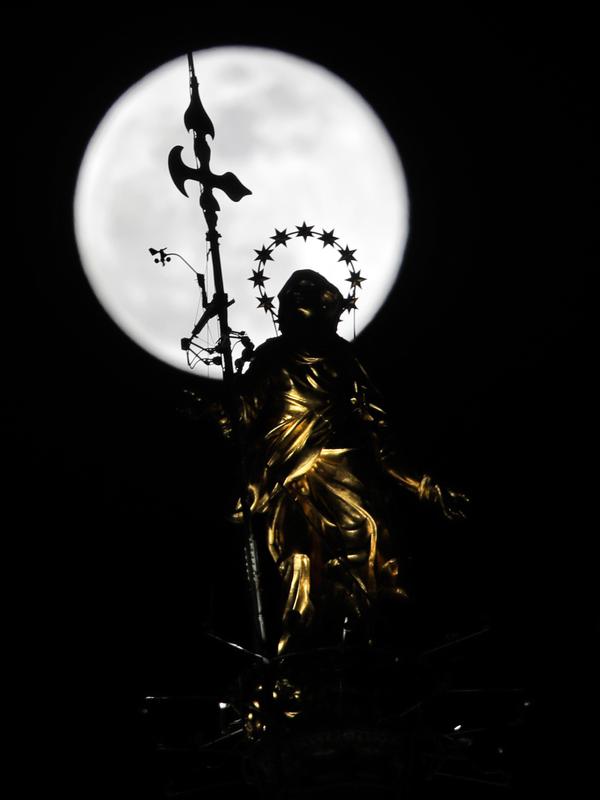 Fenomena super snow moon terlihat di belakang patung Perawan Maria 'Madonnina' di atas Katedral Duomo, Milan, Italia, Selasa (19/2). Super snow moon membuat langit berada di paras paling terang sepanjang tahun. (AP Photo/Luca Bruno)