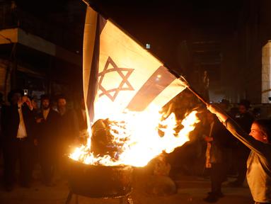 Seorang bocah Yahudi ultra ortodoks antizionis membakar bendera Israel di Yerusalem ultra-Ortodoks Mea Shearim, Rabu (2/5). Hal itu dilakukan selama perayaan Hari Raya Yahudi Lag BaOmer. (MENAHEM KAHANA / AFP)