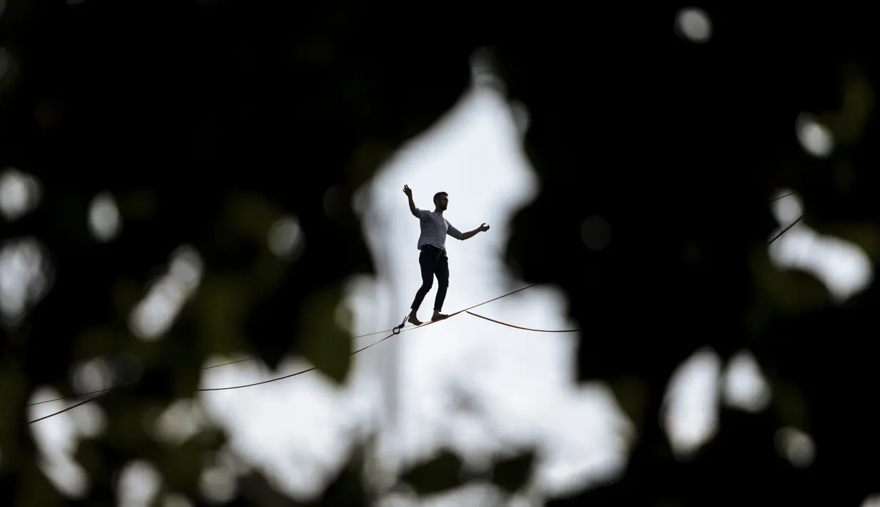 Akrobatik Prancis Nathan Paulin mencoba berjalan meniti seutas tali slackline dari Menara Eiffel melintasi Sungai Seine, di Paris, Minggu (19/9/2021). Pada 2019, pria Prancis itu melakukan slackline walk setinggi 150 meter dengan panjang 510 meter. (AP Photo/Lewis Joly)