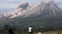 Orang-orang menyaksikan Gunung Sinabung memuntahkan material vulkanik saat meletus di Karo, Sumatera Utara, Kamis (11/3/2021). Gunung Sinabung erupsi dengan tinggi kolom 3.000 meter di atas puncak. (AP Photo/Binsar Bakkara)