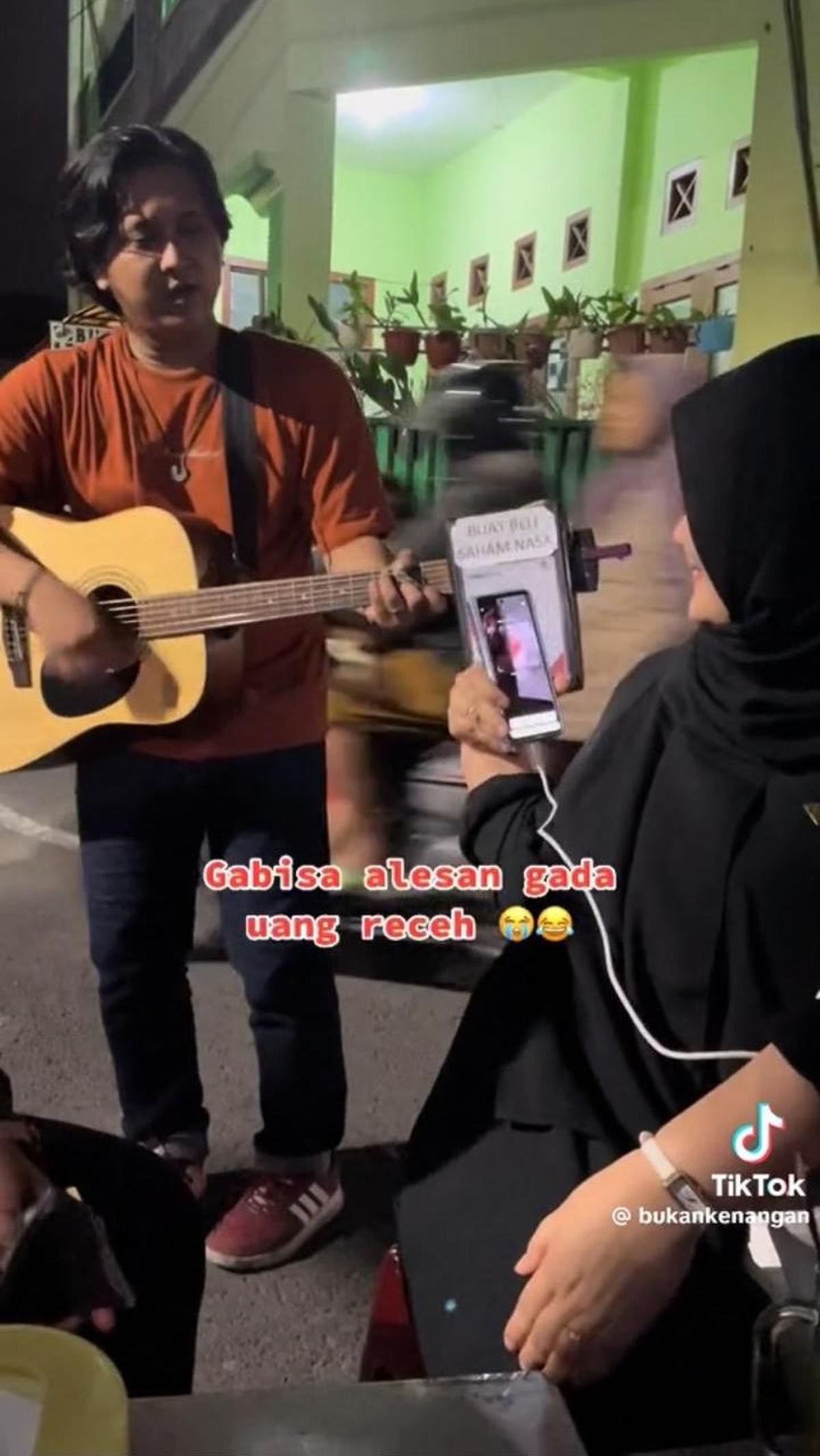 Pengamen ini pun tampak menyanyikan sebuah lagu di depan anak muda yang sedang berkumpul ini.