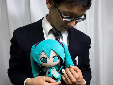 Akihiko Kondo asal Jepang berpose dengan boneka aktris virtual, Hatsune Miku sambil mengenakan cincin kawin mereka di Tokyo, 10 November 2018. Pria berusia 35 tahun itu memutuskan menikah dengan boneka anime pada 4 November lalu. (Behrouz MEHRI/AFP)