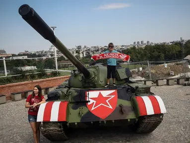 Suporter Red Star Belgrade berpose di tank T-55 yang terparkir di tribun utara Stadion Rajko Mitic, Belgrade, Serbia, Selasa (27/8/2019). Kehadiran tank tersebut memicu protes dari pihak Kroasia yang sempat berperang merebut kemerdekaannya dari Yugoslavia. (OLIVER BUNIC/AFP)