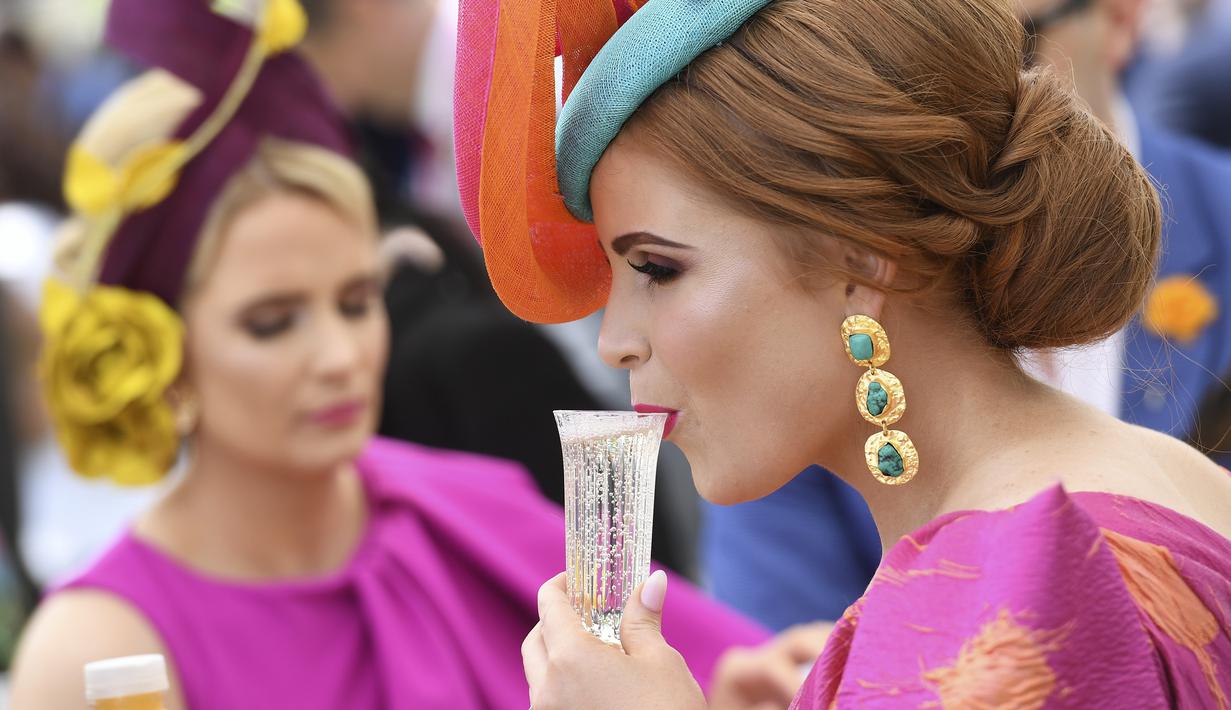 Seorang wanita minum sebelum pertandingan pacuan kuda Piala Melbourne di Melbourne (5/11/2019). Para wanita tampil cantik dan modis dengan hiasan kepala yang mereka gunakan selama menyaksikan balap kuda di Melbourne Cup.  (AFP Photo/William West)