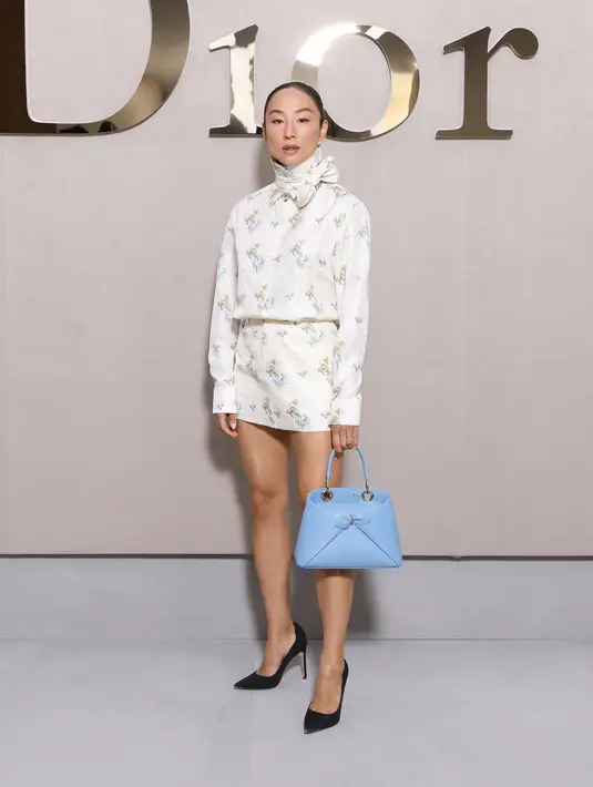 Greta Lee kenakan setelah print kemeja, rok, dan scarf ivory. Lengkap dengan heels dan tas Dior biru pastel yang kontras dengan busananya [Dior]