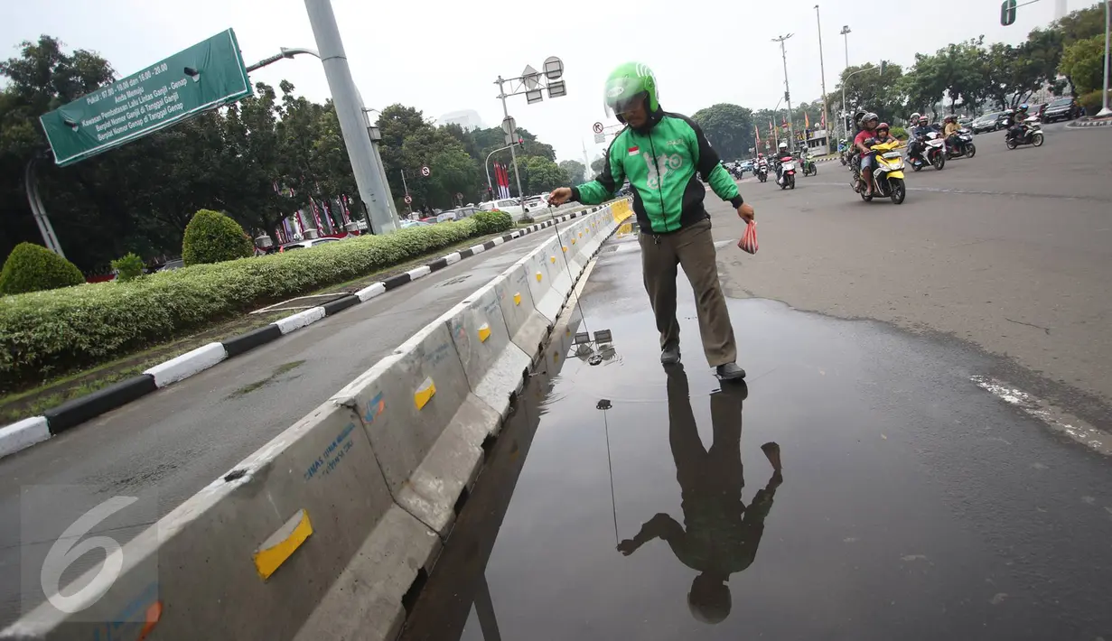 Pengendara Gojek bernama Ari mencari ranjau paku yang berserakan di sekitar Istana Negara, Jakarta, Minggu (14/8). Meskipun tak dibayar, Ari berinisiatif untuk mengumpulkan ranjau paku yang merugikan pengendara tersebut. (Liputan6.com/Immanuel Antonius)