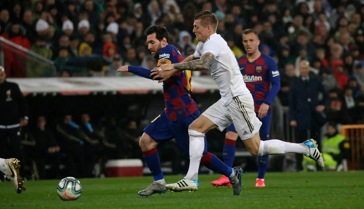 Megabintang Barcelona, Lionel Messi, berebut bola dengan pemain Real Madrid, Toni Kroos pada lanjutan pertandingan La Liga di Santiago Bernabeu, Minggu (2/3/2020).  Real Madrid membungkam Barcelona 2-0 dan merebut puncak klasemen dari Barcelona. (AP/Andrea Comas)