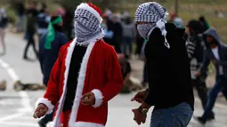 Seorang demonstran Palestina mengenakan kostum Santa Claus bersiap melempar batu ke arah pasukan keamanan Israel saat terjadi bentrokan di pos pemeriksaan Atarot di pinggiran utara Yerusalem (19/12). (AFP Photo/Abbas Momani)