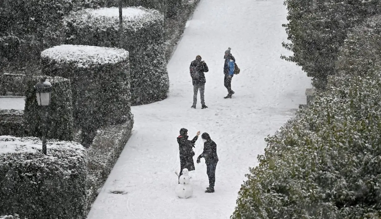 Orang-orang membuat manusia salju di Taman Sabatini di luar Istana Kerajaan, Madrid, Spanyol, Jumat (8/1/2021). Badai Filomena mengakibatkan salju lebat turun di Madrid dan seluruh Spanyol. (GABRIEL BOUYS/AFP)