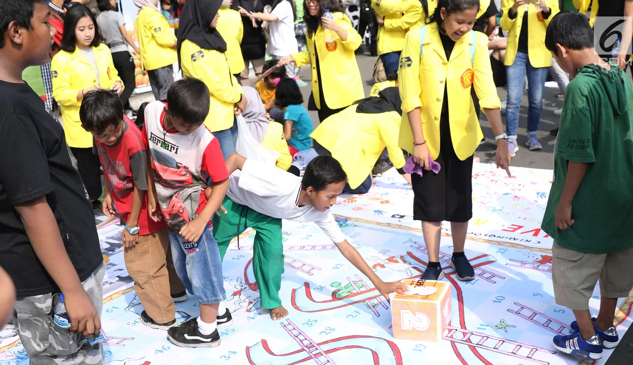 Mahasiswa jurusan Kriminologi Fisip UI mendampingi anak-anak bermain ular tangga saat gelaran Car Free Day di kawasan Bundaran HI, Jakarta, Minggu (18/11). Permainan ini bertujuan mengurangi anak-anak bermain gawai. (Liputan6.com/Helmi Fithriansyah)