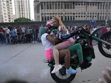 Pengendara sepeda motor, dengan dua penumpang wanita, melakukan wheelie di sepeda motornya selama pameran di lingkungan El Valle Caracas, Venezuela, Sabtu (31/7/2021). (AP Photo/Ariana Cubillos)