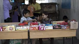 Anak-anak Palestina duduk di depan warung yang berada di kamp pengungsi Sekolah PBB di Jabalia, Gaza (28/7/14). (AFP PHOTO/MOHAMMED ABED)