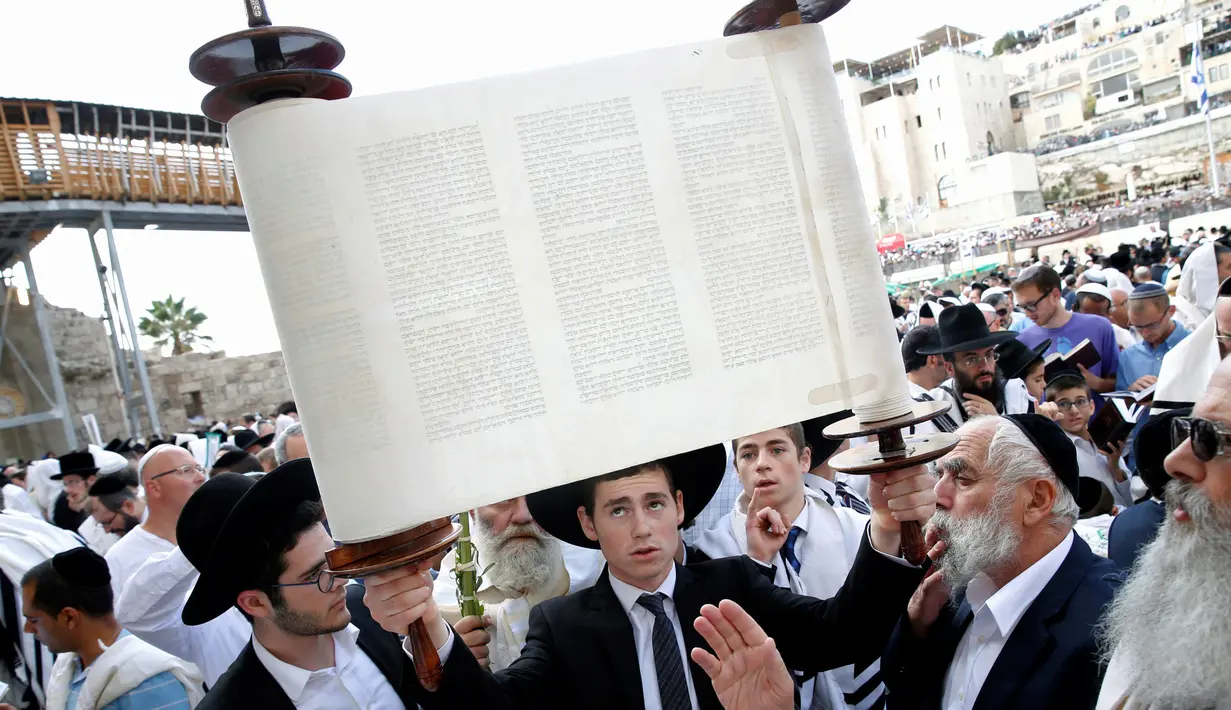 Seorang umat Yahudi memegang gulungan Taurat saat mengikuti doa massal selama liburan Sukkot di depan Tembok Ratapan di Kota Tua Yerusalem, (19/10). (REUTERS/Baz Ratner)