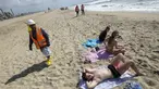 Seorang pekerja berjalan saat pengunjung pantai beristirahat di Huntington Beach, California, Senin (11/10/2021). Pantai Huntington membuka kembali garis pantainya setelah hasil pengujian air kembali dengan jumlah racun terkait minyak yang tidak terdeteksi di air laut. (AP Photo / Ringo HW Chiu)