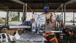 Seniman Thiago Mundano memegang salinan "The Coffee Farmer" karya mendiang pelukis Brasil Candido Portinari dan versi skala kecil dari muralnya "The Forest Brigadier" di Sao Paulo, Jumat (15/10/2021). Mundano mencampur abu kebakaran hutan di seluruh Brasil ke dalam catnya. (AP/Marcelo Chello)