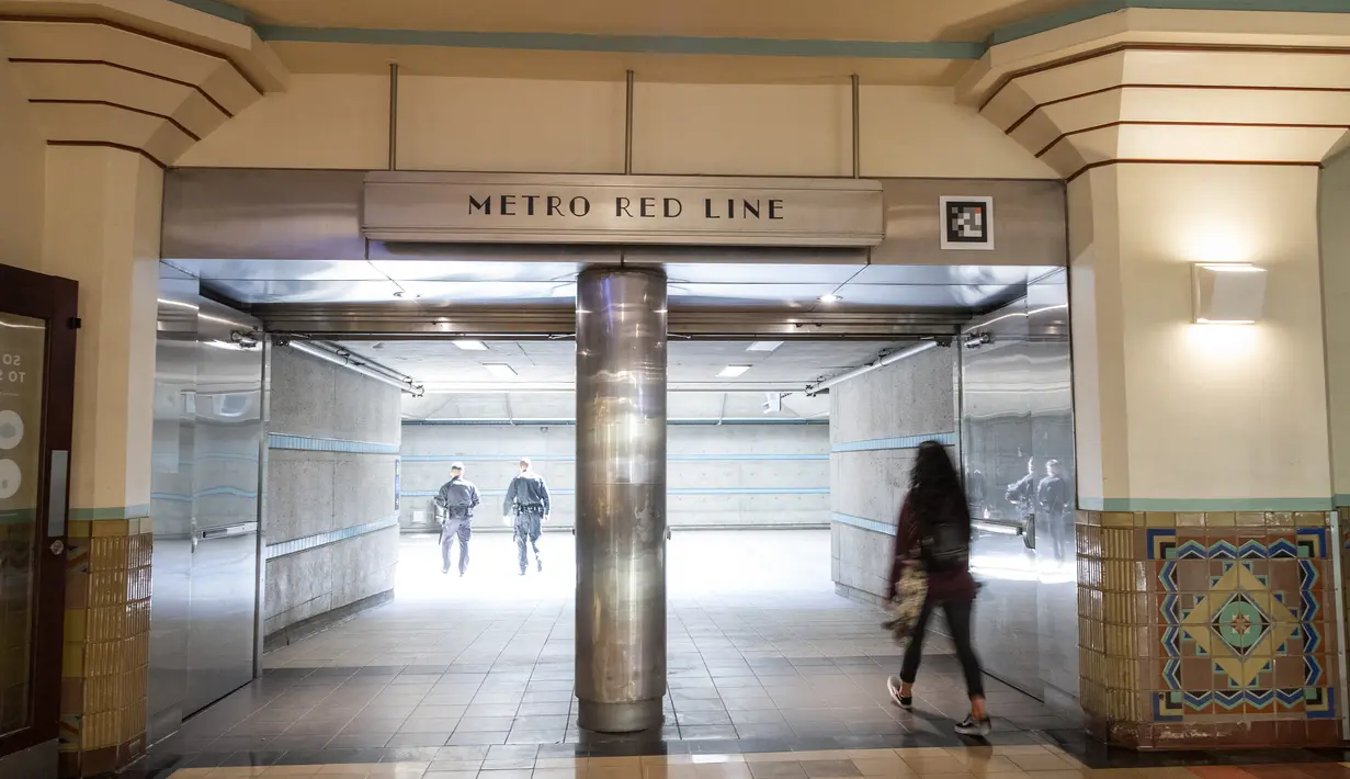 Polisi terlihat di peron saat penumpang berjalan melalui pintu masuk Red Line di Union Station, pusat kota Los Angeles, Rabu (17/3/2021). Penyelenggara Academy Awards ke-93 atau Oscars 2021 akan digelar di dua lokasi berbeda, yakni Dolby Theater dan stasiun kereta Union Station. (VALERIE MACON/AFP)