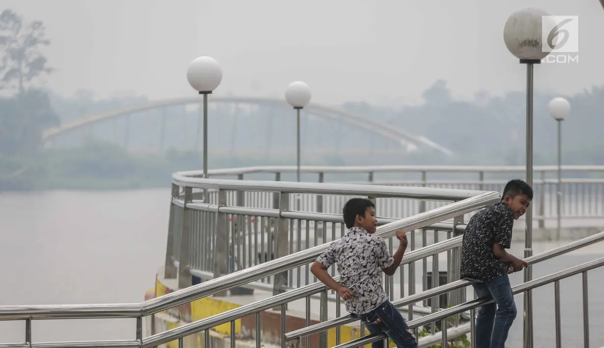 Anak-anak bermain saat asap kebakaran lahan gambut menyelimuti alun-alun Kabupaten Siak, Riau, Kamis (12/9/2019). Asap pekat kebakaran lahan gambut tersebut selain mengganggu kesehatan serta mencemari udara sehingga kualitasnya turun ke status tidak sehat. (Liputan6.com/Faizal Fanani)