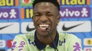 Vinicius Junior tertawa geli karena ulah si kucing yang tiba-tiba jadi penyusup di konferensi pers timnya. (AP/Andre Penner)