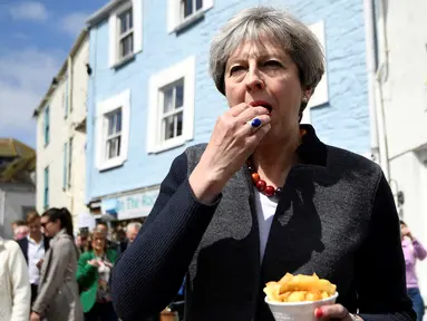 Perdana Menteri (PM) Inggris, Theresa May mencicipi beberapa keripik saat berhenti untuk kampanye di Mevagissey, Cornwall, Selasa (2/5). Theresa May melakukan kampanye dengan berkeliling jalanan di Cornwall. (Dylan Martinez/PA via AP)