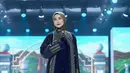 Desy Ratnasari tampil memancarkan aura elegan yang tenang dalam balutan busana bernuansa gelap, perpaduan hitam dan biru navy yang terasa sophisticated. Siluetnya dibuat lurus dan memanjang, dengan inner dress bertekstur pleats halus berwarna biru tua yang memberi efek jatuh ringan setiap kali ia melangkah. Di bagian luar, ia mengenakan outer panjang berpotongan clean dengan panel bordir vertikal bernuansa emas-keperakan. [Dok/Shi by Shireen & Zaskia Sungkar].