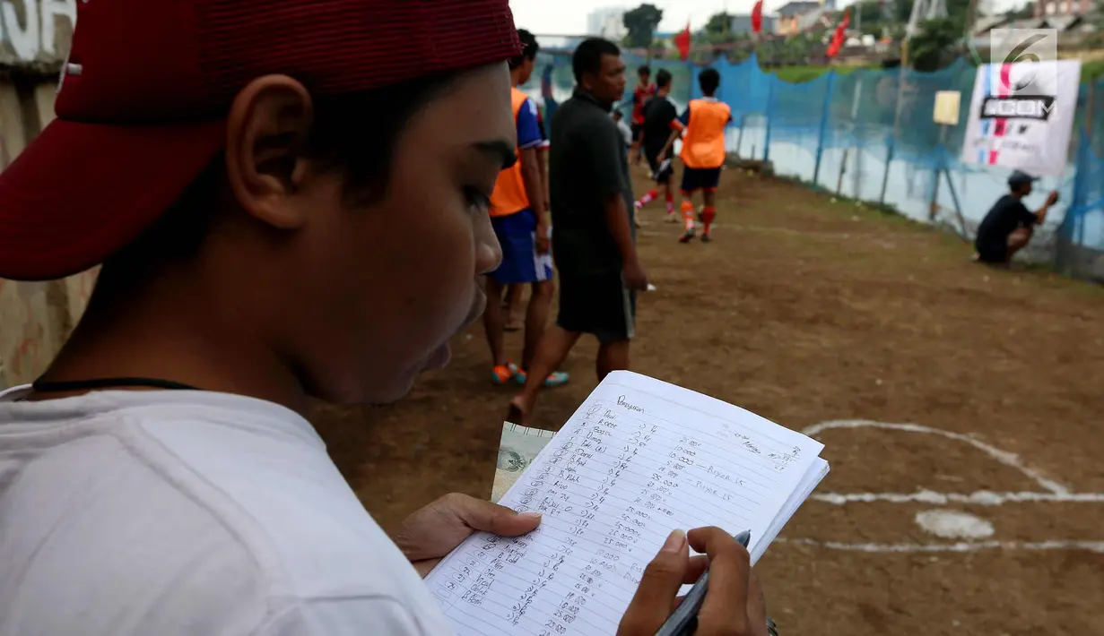 Warga mencatat tim yang ikut dalam kompetisi sepak bola di pinggir Kali Banjir Kanal Barat, Jakarta, Sabtu (5/11). Minimnya sarana bermain sepak bola mengakibatkan warga terpaksa memanfaatkan lahan di pinggir kali. (Liputan6.com/Johan Tallo)