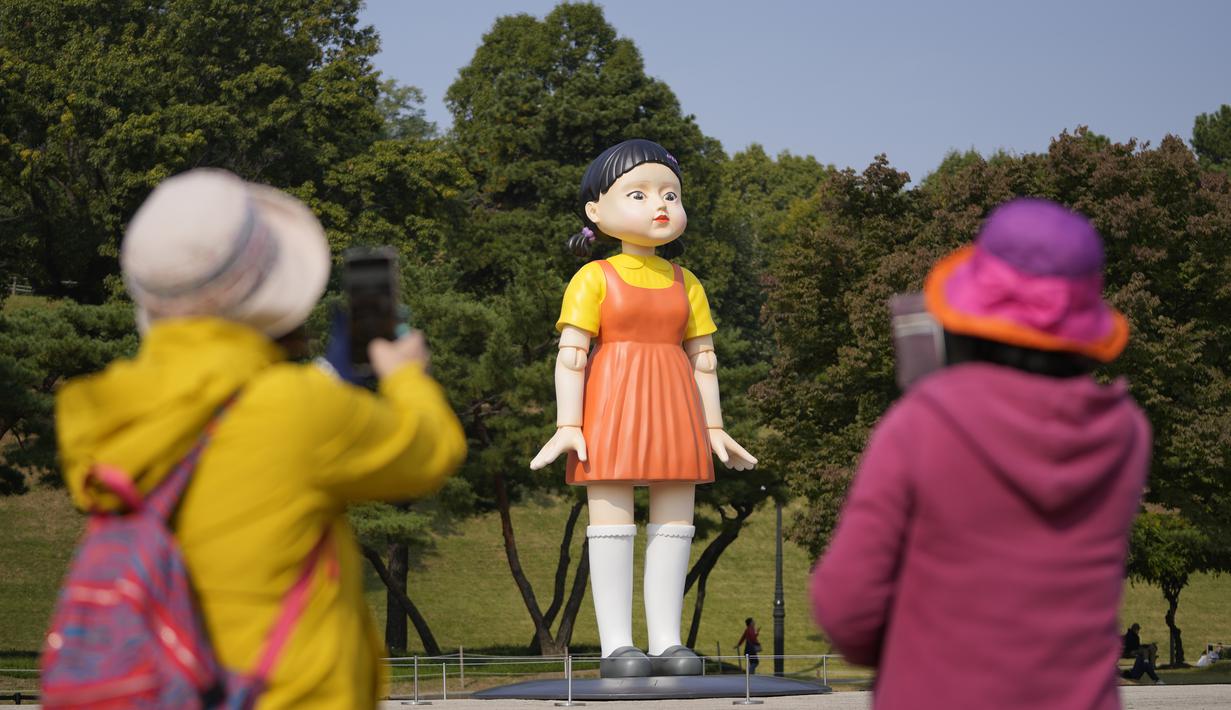 Pengunjung mengambil foto dekat boneka 'Younghee' yang menjadi maskot dalam serial Netflix asal Korea, Squid Game, di Olympic park, Seoul, Selasa (26/10/2021). Boneka setinggi empat meter atau 13 kaki itu, akan dipamerkan di taman tersebut selama tiga bulan. (AP Photo/Lee Jin-man)