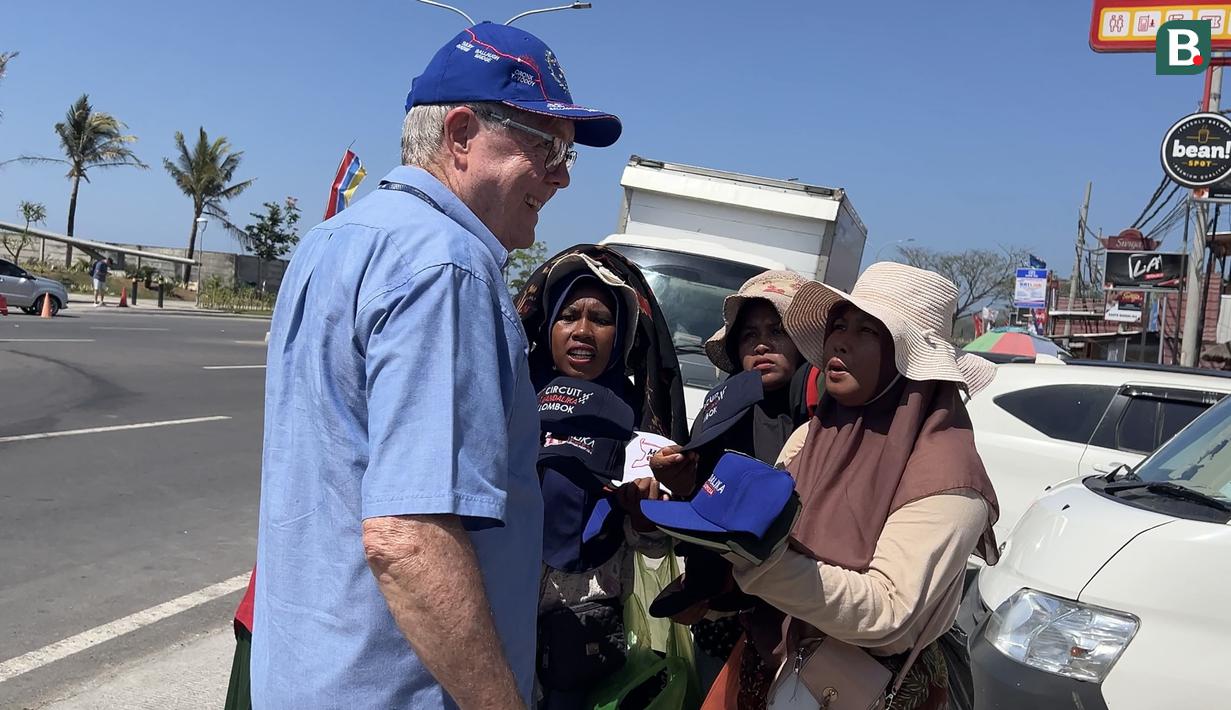Sejumlah pedagang lokal ikut menjajakan aksesoris balap kepada seorang wisatawan di sekitar Sirkuit Mandalika, Lombok, Sabtu (14/10/2023) menjelang berlangsungnya balapan utama ajang MotoGP Mandalika 2023 yang akan digelar Minggu, 15 Oktober 2023. (Bola.com/Benediktus Gerendo Pradigdo)