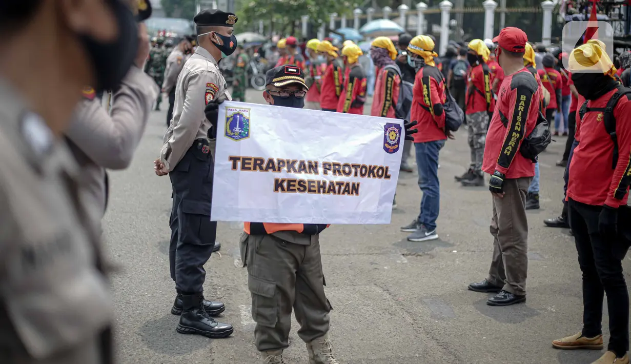Petugas Satpol PP memegang poster imbauan protokol kesehatan COVID-19 saat unjuk rasa buruh di depan Gedung DPR, Jakarta, Selasa (17/11/2020). Pemerintah terus mengingatkan pentingnya 3M yaitu memakai masker, menjaga jarak, dan mencuci sebagai upaya pencegahan Covid-19. (Liputan6.com/Faizal Fanani)