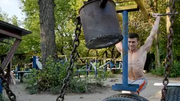 Mikhail (21) melakukan latihan angkat beban di sebuah gym outdoor di Ibu Kota Ukraina, Kiev, 18 Agustus 2017.. Alat olahraga di taman Kachalka itu dibuat dari rangka tank dan beberapa alat lainnya dia buat dari bagian kapal perang. (GENYA SAVILOV/AFP)