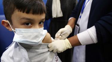 Petugas kesehatan menyuntikkan vaksin covid-19 Pfizer-BioNTech kepada seorang anak di pusat vaksinasi di Kuwait International Fairground di Kuwait City pada 3 Februari 2022. Kementerian kesehatan Kuwait mulai memvaksinasi anak usia 5 hingga 11 tahun. (YASSER AL-ZAYYAT / AFP)