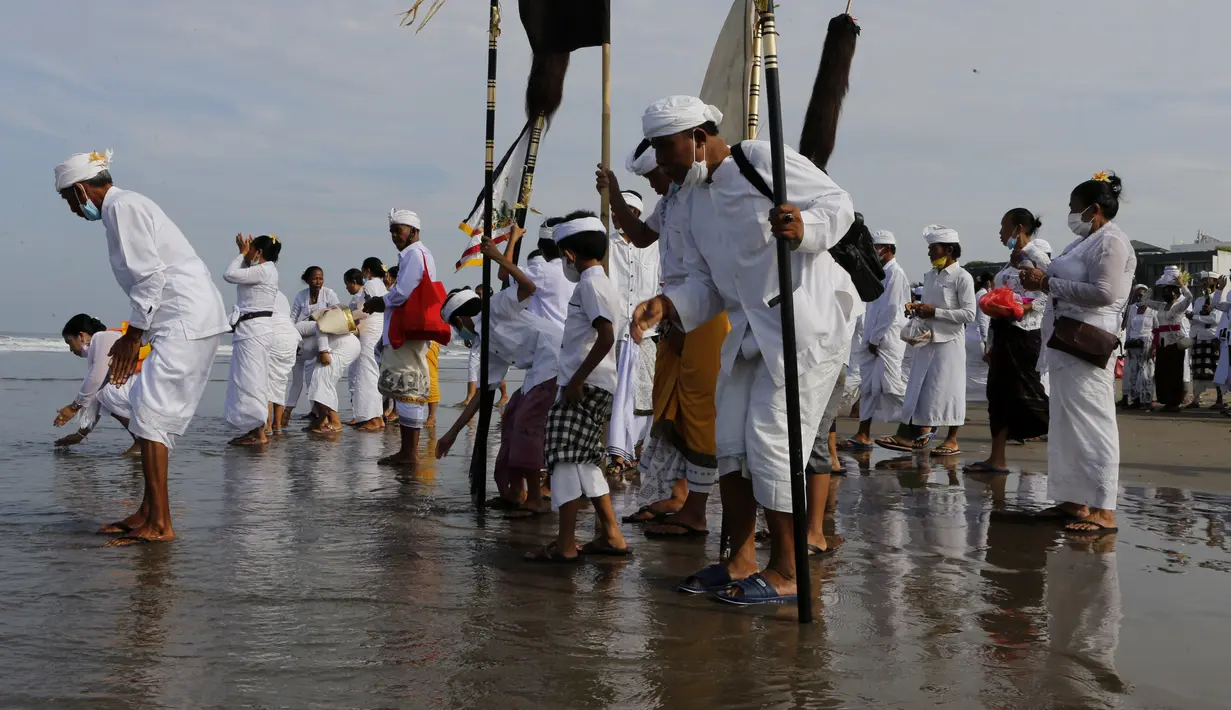 Orang-orang mencelupkan kaki mereka di laut selama ritual Melasti di Bali, Senin (28/2/2022). Ritual yang dilakukan menjelang Hari Raya Nyepi umat Hindu ini diadakan untuk menyucikan alam semesta dari pengaruh buruk, perbuatan dan pikiran buruk. (AP Photo/Firdia Lisnawati)