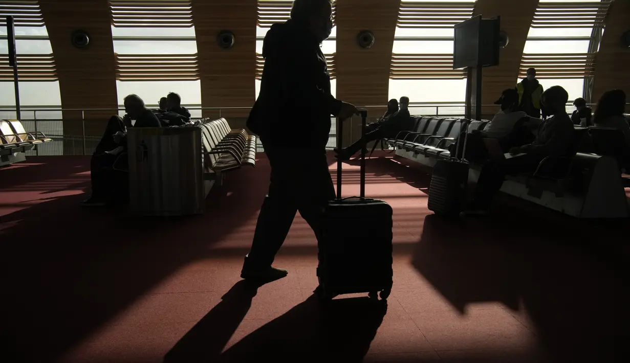 Seorang penumpang Amerika Serikat membawa barang bawaannya di ruang tunggu sebelum menaiki pesawat di bandara Charles de Gaulle, utara Paris, Senin (8/11/2021). (AP Photo/Christophe Ena)