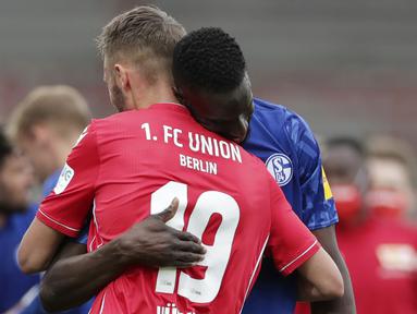 Pemain Union Berlin, Florian Huebner, berpelukan dengan pemain Schalke, Salif Sane, pada laga Bundesliga di Weserstadion Minggu (7/6/2020). Kedua tim bermain imbang 1-1. (AP/Michael Sohn)