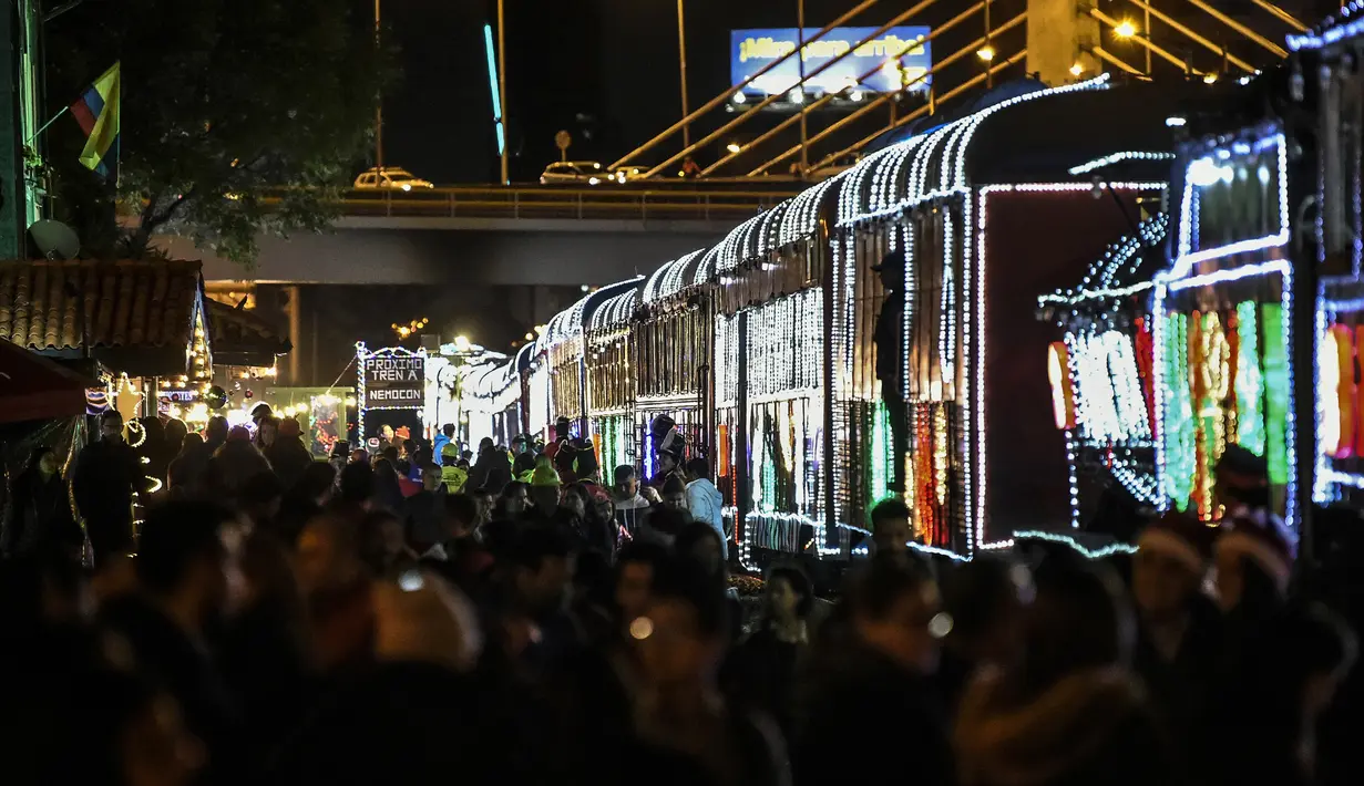Sejumlah penumpang bersiap untuk naik kereta wisata yang dihiasi lampu Natal di Bogota (20/12/2019). Meyambut Hari Natal, kereta wisata di Kolombia membuat cara unik dengan memasangkan lampu warna-warni agar menjadi daya tarik penumpang. (AFP Photo/Juan Barreto)