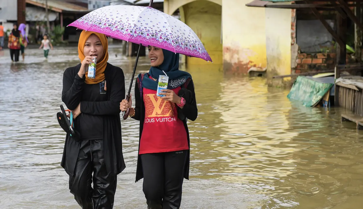 Warga melintasi jalan yang tergenang air di kawasan Rantau Panjang, Malaysia, Kamis (5/1). , Malaysia, Kamis (5/1). Hujan lebat dalam lima hari juga telah menyebabkan 101 sekolah ditutup. (AFP PHOTO / MOHD RASFAN)