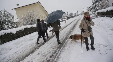 Orang-orang berjalan dengan anjing mereka di salju di Burguete, Spanyol utara, Senin, 16 Januari 2023. Pihak berwenang telah mengumumkan salju dan suhu sangat rendah selama beberapa hari ke depan di seluruh bagian utara negara itu. (AP Photo/Alvaro Barrientos)