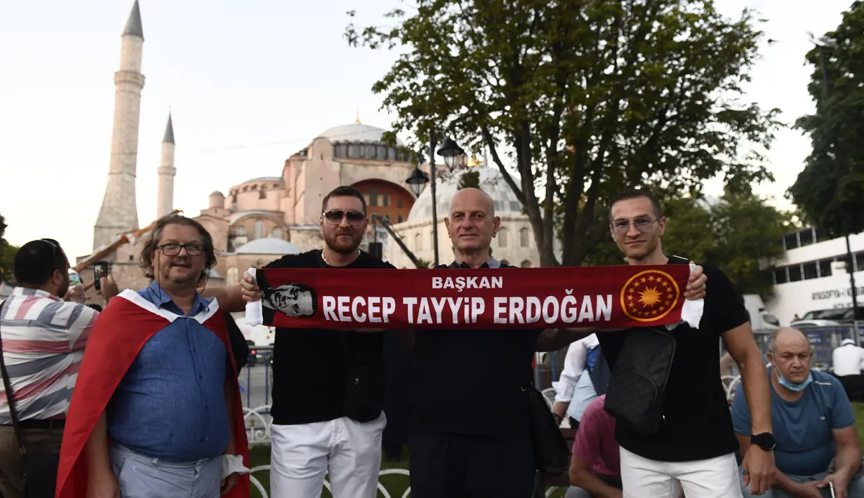 Orang-orang memegang syal dengan nama Presiden Turki Recep Tayyip Erdogan, ketika foto di luar era Bizantium Hagia Sophia, di distrik bersejarah Sultanahmet Istanbul, Kamis, (23/7/2020). Bangunan bersejarah itu resmi dialih fungsi dari museum menjadi masjid pada 10 Juli lalu. (AP Photo/Omer Kuscu)