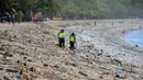 Polisi berdiri di antara sampah kiriman yang terdampar memenuhi pesisir pantai Kuta, Bali, Kamis (31/12/2020). Menjelang pergantian tahun baru, Pantai Kuta hanya terlihat beberapa wisatawan, namun tumpukan sampah kiriman tersebar di sepanjang bibir pantai. (SONNY TUMBELAKA / AFP)