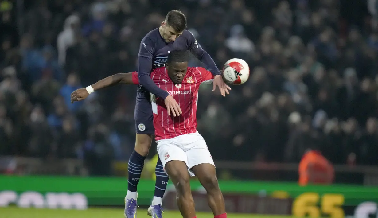 Bek Manchester City Ruben Dias melompat di atas penyerang tim divisi 4 Swindon Town, Tyreece Simpson dalam duel putaran ketiga Piala FA 2021/22 di County Ground, Sabtu (8/1/2022) dini hari WIB. Manchester City menang telak 4-1 saat menghadapi Swindon Town. (AP Photo/Kirsty Wigglesworth)