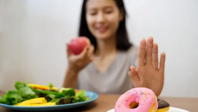 Seorang perempuan menolak sepiring donat dan hendak memakan buah serta sayuran (Foto Dok: Freepik/skawee)