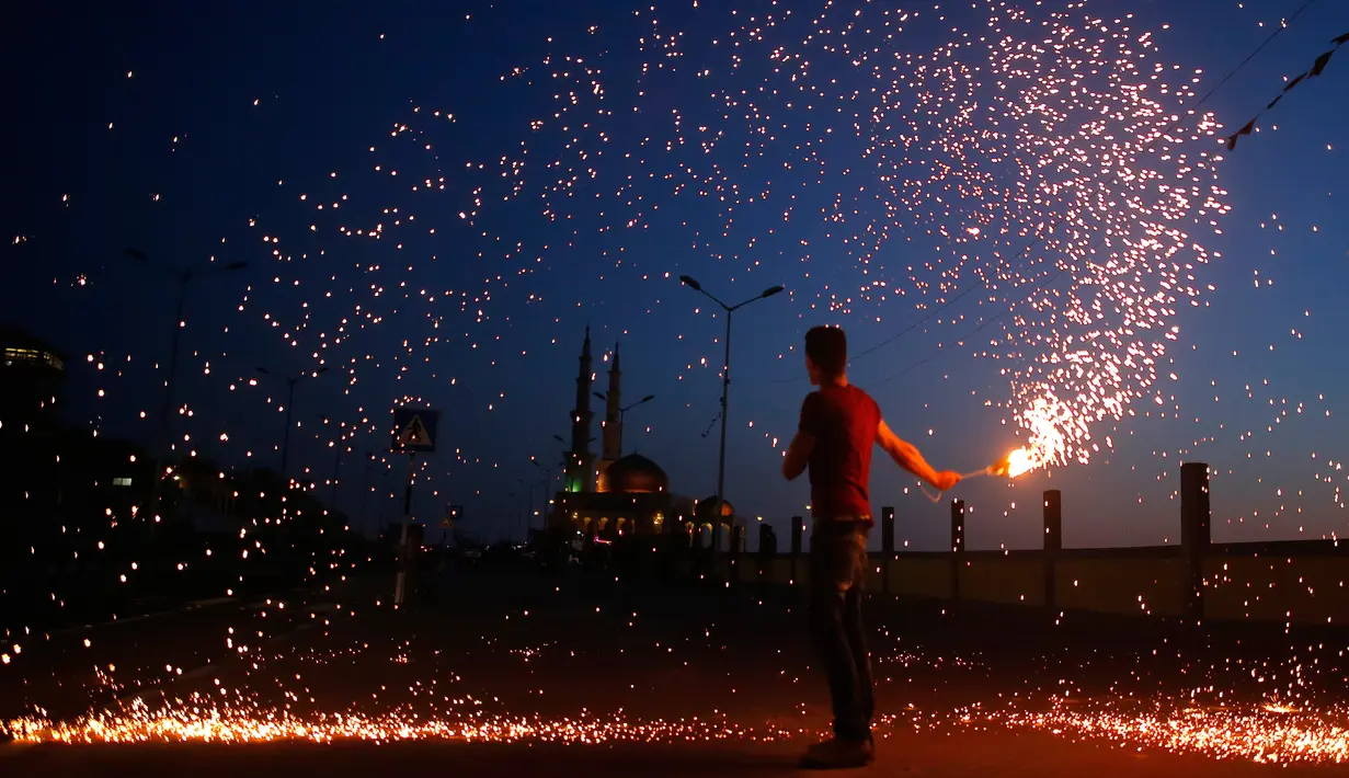 Seorang pemuda Palestina mengayunkan kembang api di depan sebuah masjid di Kota Gaza, Palestina (16/5). Mereka bermain kembang api untuk menyambut puasa pertama di bulan Ramadan. (AFP Photo/Mohammed Abed)