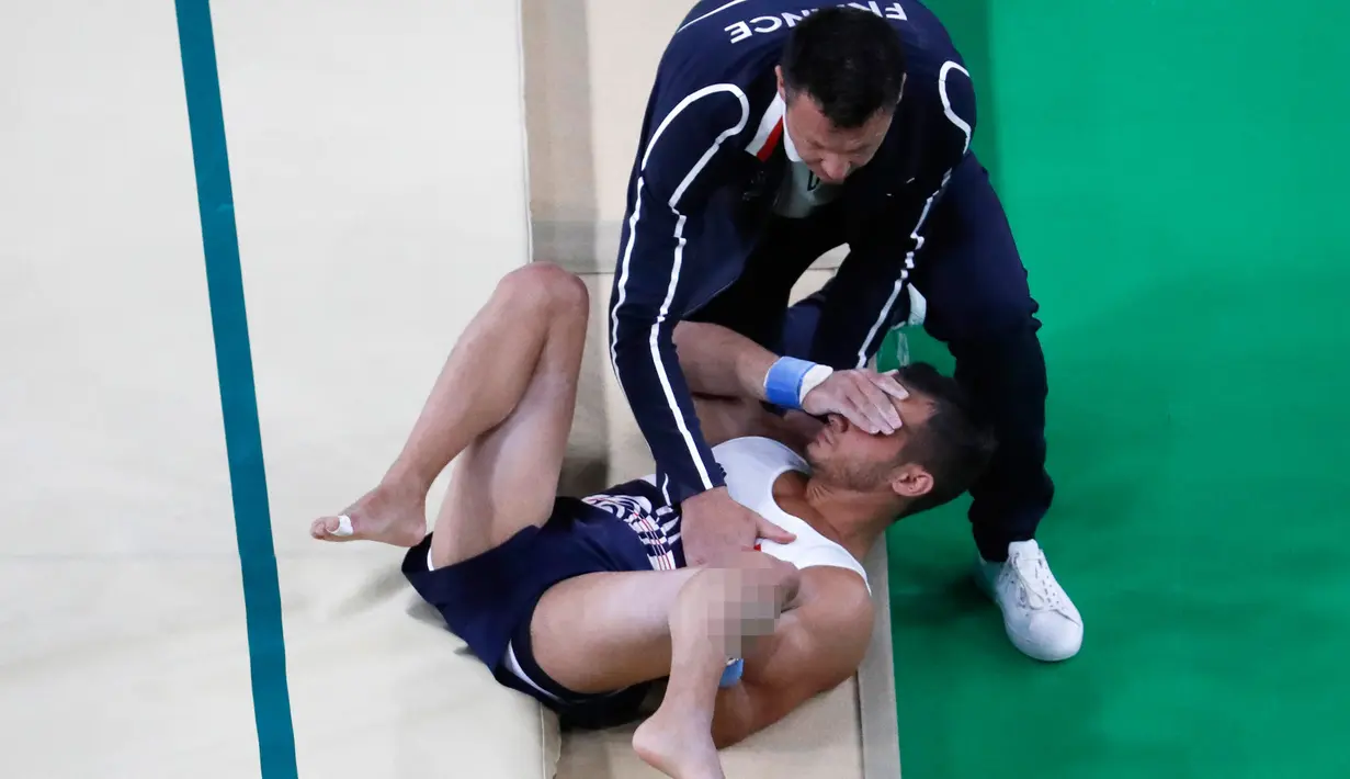 Seorang pelatih membantu atlet senam artistik Prancis Samir Ait Said setelah mengalami cedera pada babak kualifikasi Olimpiade Rio 2016 di Rio Olympic Arena, Brasil, Minggu (7/8). Samir gagal mendarat dan membuat kaki kirinya patah. (Thomas COEX/AFP)