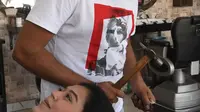 Dalam gambar pada 8 April 2021, tukang cukur Pakistan Ali Abbas menggunakan palu dan pisau daging untuk memotong rambut pelanggan di tokonya di Lahore. Berharap membuktikan kemampuannya dalam persaingan, Ali Abbas mengandalkan berbagai alat yang tidak biasa untuk melatih keahliannya. (Arif ALI/AFP)