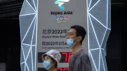Orang-orang yang memakai masker untuk melindungi diri dari COVID-19 berjalan melewati layar yang menunjukkan jam hitung mundur ke Olimpiade Musim Dingin 2022 di Beijing (18/8/2021).  Pejabat tinggi Beijing menegaskan kembali perlunya anti-pencegahan yang ketat. (AP Photo/Mark Schiefelbein)